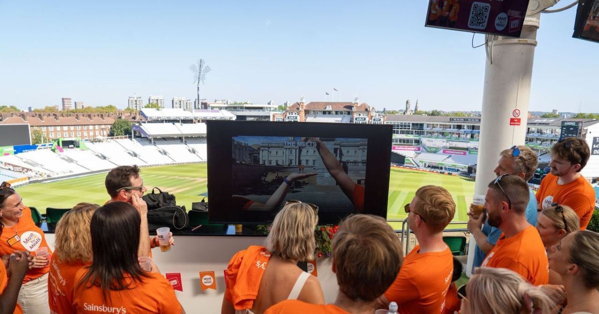 Participants in orange Sainsbury's T-shirts watching team photos on a big screen at The Oval cricket ground during the debrief of their Comic Relief GPS Treasure Hunt in London