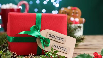Close-up van een rood ingepakt kerstcadeau met een groen satijnen lint en een label met de tekst "SECRET SANTA", op een feestelijke, licht onscherpe achtergrond.