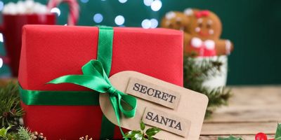 Close-up van een rood ingepakt kerstcadeau met een groen satijnen lint en een label met de tekst "SECRET SANTA", op een feestelijke, licht onscherpe achtergrond.
