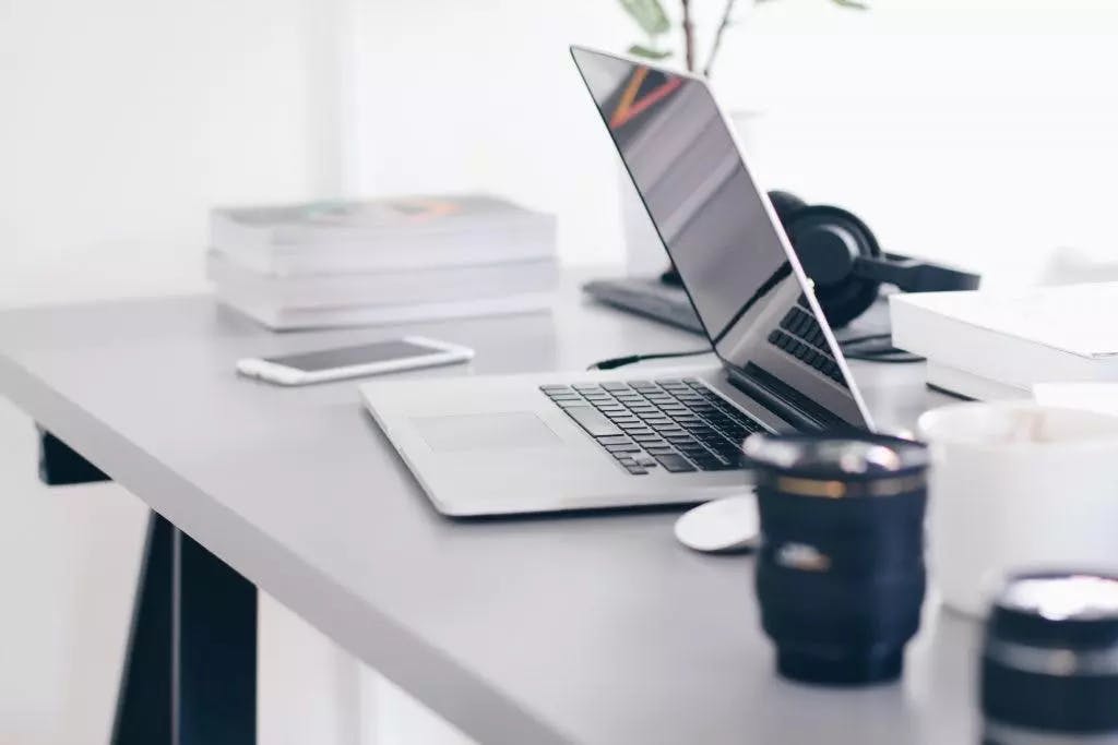 Un espace de travail moderne et minimaliste avec un ordinateur portable ouvert, un smartphone, une pile de livres et une paire d'écouteurs sur un bureau gris épuré.