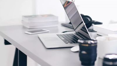 Een moderne, minimalistische werkplek met een open laptop, een smartphone, een stapel boeken en een koptelefoon op een strakke grijze bureau.