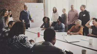 A large, diverse group of smiling people gathered around a long conference table for a collaborative business workshop or team meeting.