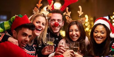 Een vrolijke groep van vijf vrienden die lachend klinken op een kerstfeest, gekleed in feestelijke outfits zoals rendiergewei, een kerstmuts, een elfenmuts en kersttrui.