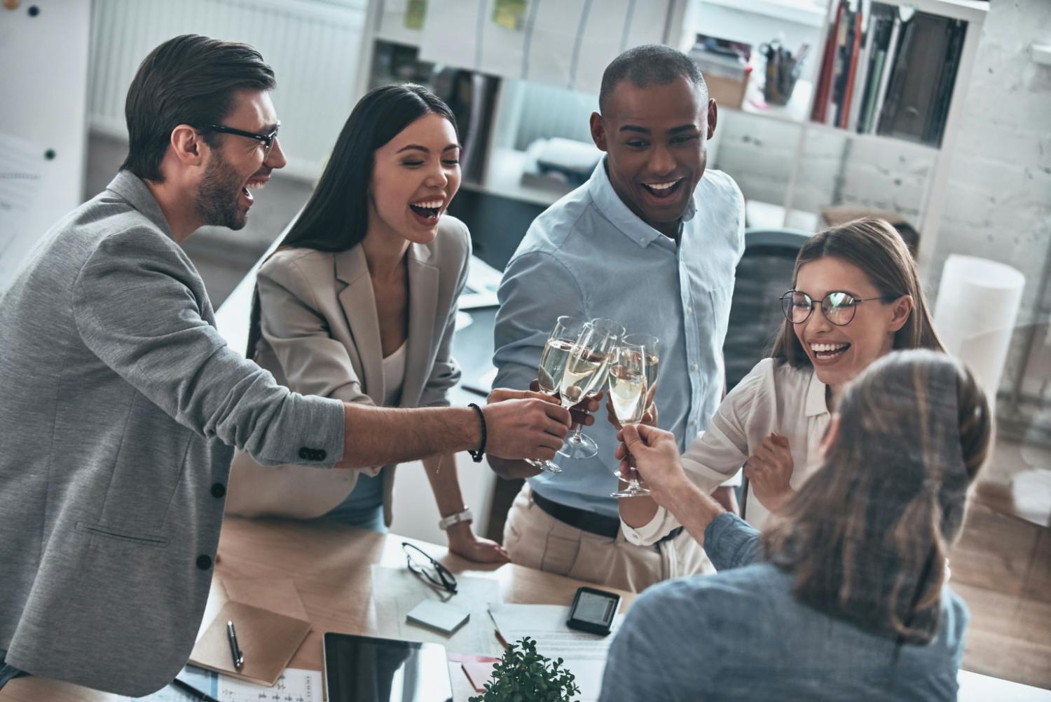 Vue en plongée d'un groupe diversifié de cinq collègues souriants portant un toast avec des flûtes de champagne pour célébrer un succès dans leur bureau.