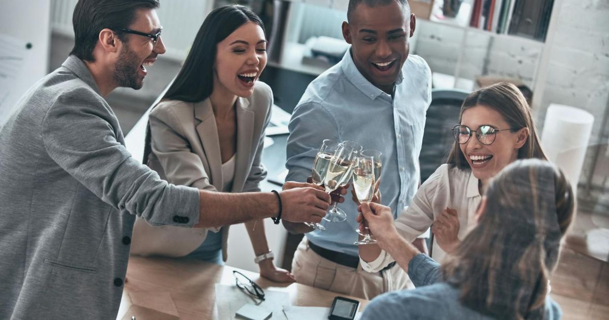 A high-angle view of a diverse group of five smiling colleagues clinking champagne flutes together to celebrate a success in their office.