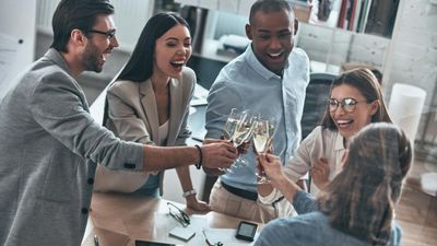 Bovenaanzicht van een diverse groep van vijf glimlachende collega's die klinken met champagnefluiten om een succes te vieren in hun kantoor.
