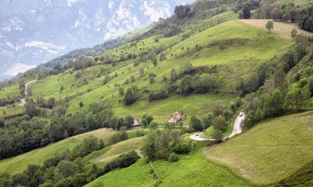 A rural mountain scene in France with a small house and a winding road surrounded by greenery