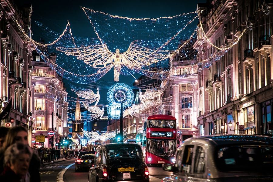 A night view of Regent Street in London during the holiday season, illuminated by large, glowing angel Christmas lights spanning across the busy road filled with black cabs and a red double-decker bus.
