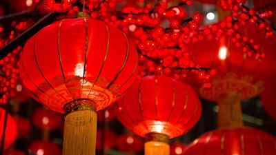 Een close-up van gloeiende rode Chinese lantaarns met gouden kwasten die hangen tussen rode bloesemdecoraties, typisch gebruikt voor Chinees Nieuwjaar.