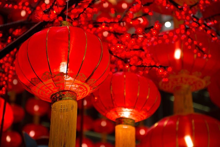 Een close-up van gloeiende rode Chinese lantaarns met gouden kwasten die hangen tussen rode bloesemdecoraties, typisch gebruikt voor Chinees Nieuwjaar.