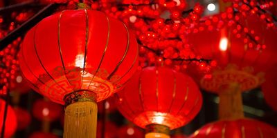 Een close-up van gloeiende rode Chinese lantaarns met gouden kwasten die hangen tussen rode bloesemdecoraties, typisch gebruikt voor Chinees Nieuwjaar.