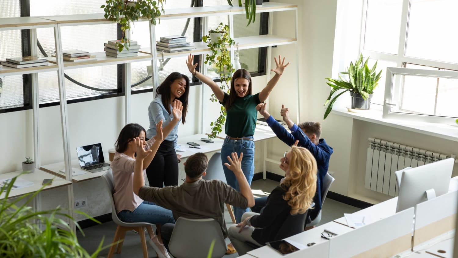 Vue en plongée d'une équipe créative de six collègues célébrant un succès dans un bureau lumineux, les mains levées, souriant et applaudissant ensemble.