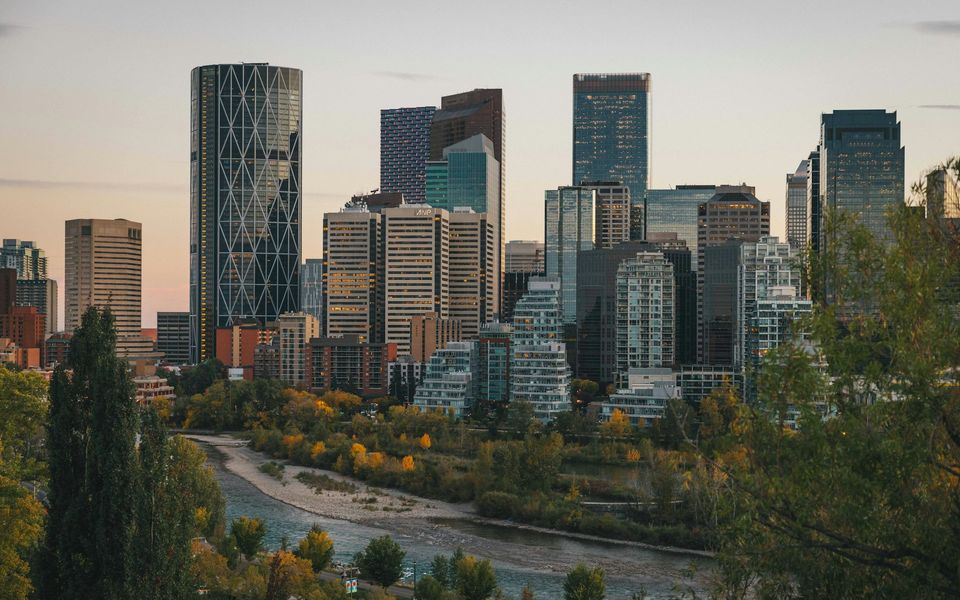 La ligne d'horizon du centre-ville de Calgary au crépuscule au-dessus de la rivière Bow, bordée d'arbres d'automne