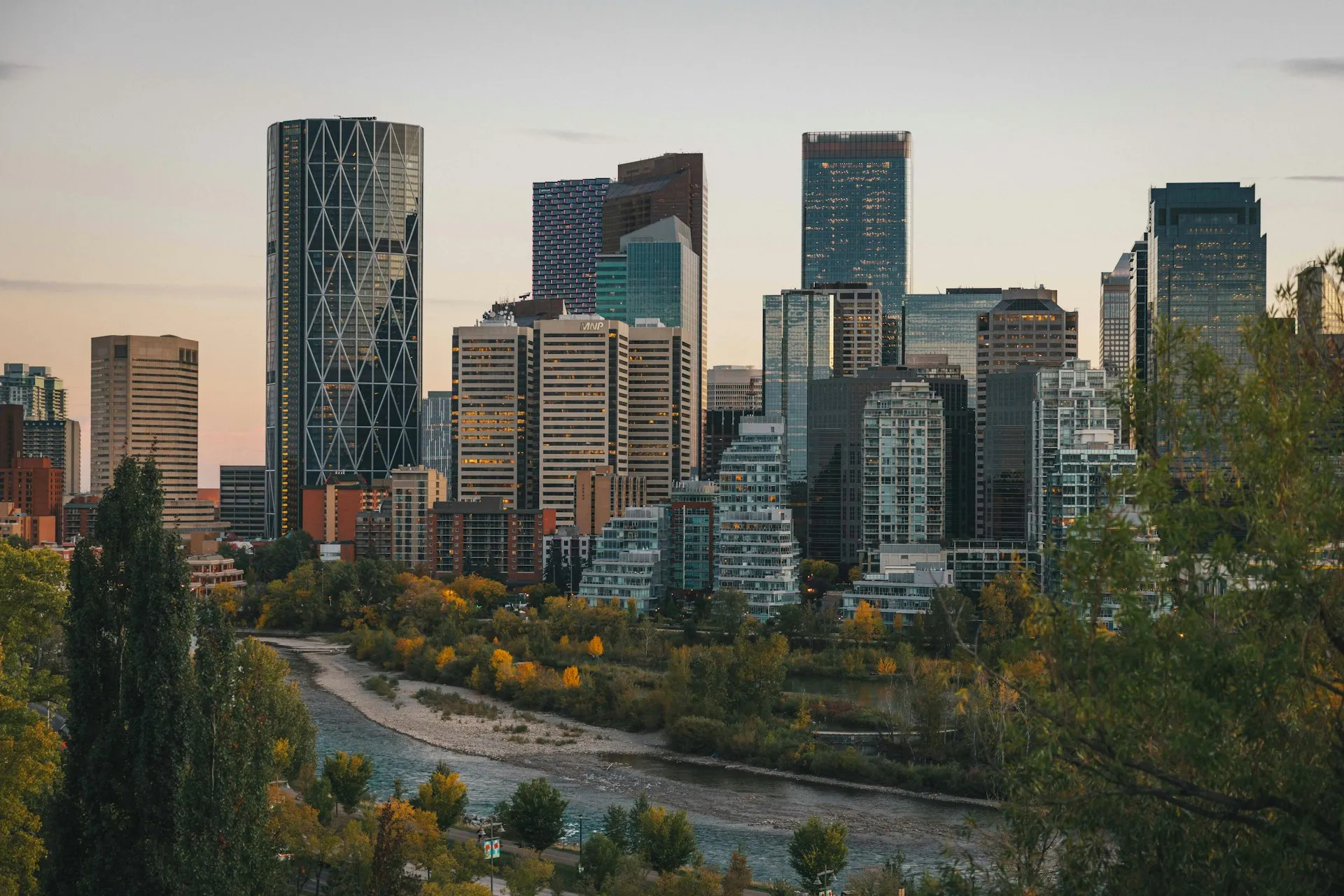 La ligne d'horizon du centre-ville de Calgary au crépuscule au-dessus de la rivière Bow, bordée d'arbres d'automne